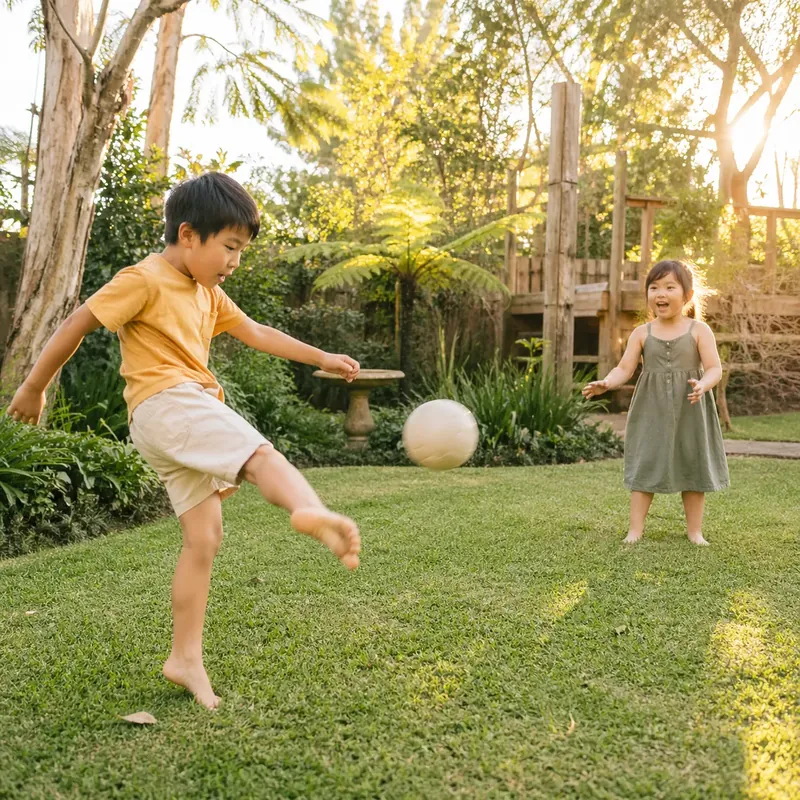Five-year-old boy mid-kick of a soft soccer ball on a backyard lawn at golden hour
